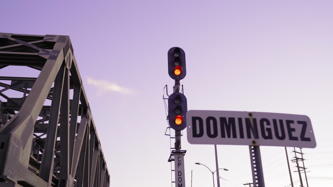 Passing by a railway light with a purple sky and a railroad bridge in the background.