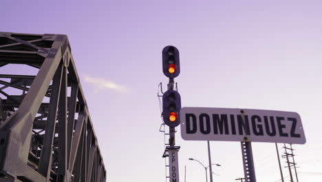 passing by a railway light with a purple sky and a railroad bridge in the background.