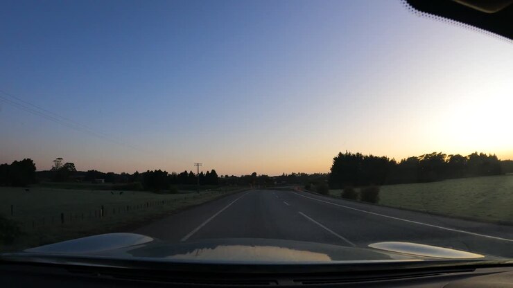 Car Driving On Asphalt Road Through Rural Fields At Sunset