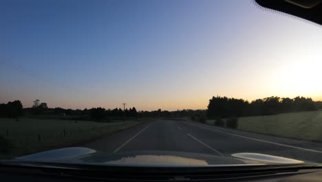 car driving on asphalt road through rural fields at sunset