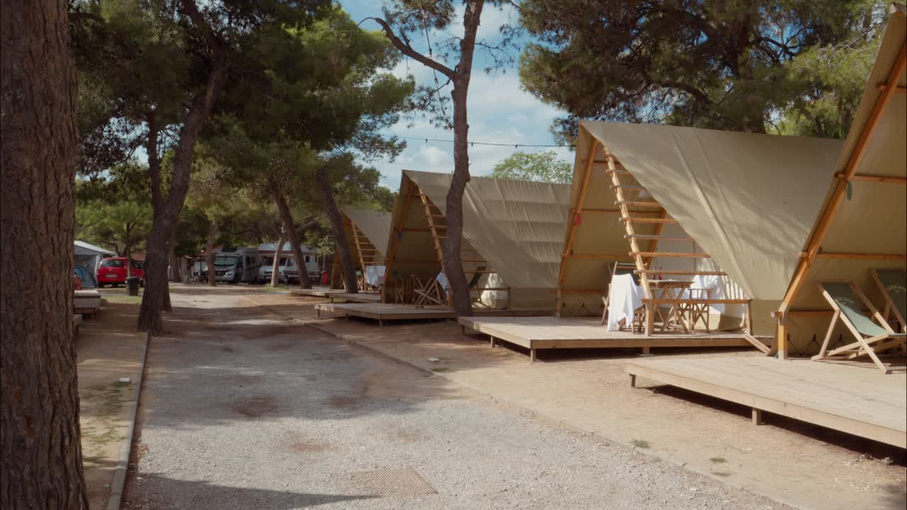 Række af glampingtelte med træplatforme på en skyggefuld campingplads