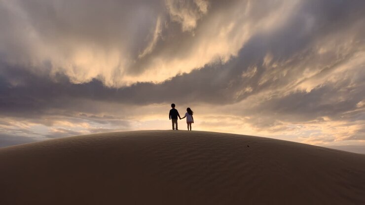 Children holding hands on a sand dune at sunset