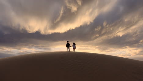 children holding hands on a sand dune at sunset