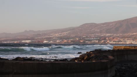 Hermosa-Vista-De-Las-Olas-Rompiendo-En-La-Costa-Con-Una-Ciudad-Al-Fondo,-Tenerife