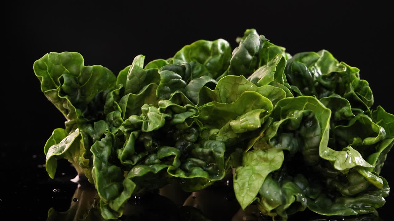 A rotating display of fresh bok choy on a reflective black surface with dramatic lighting