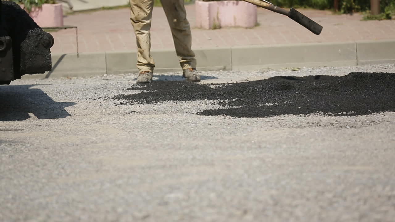 Worker Leveling Fresh Asphalt. Construction workers during asphalting road works