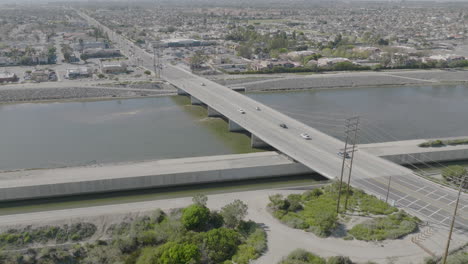 Toma-Aérea-De-Sobrevuelo-De-Autos-Que-Pasan-Por-Un-Puente-Sobre-Un-Río-En-Costa-Mesa,-California