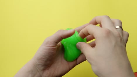 person holding green slime in hands, yellow background