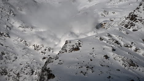 a large avalanche made with power goes down a rocky swiss alps mountain next to ski slopes, science