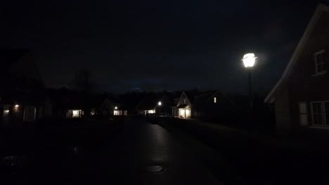 night view of a quiet residential street illuminated by house lights and street lamps