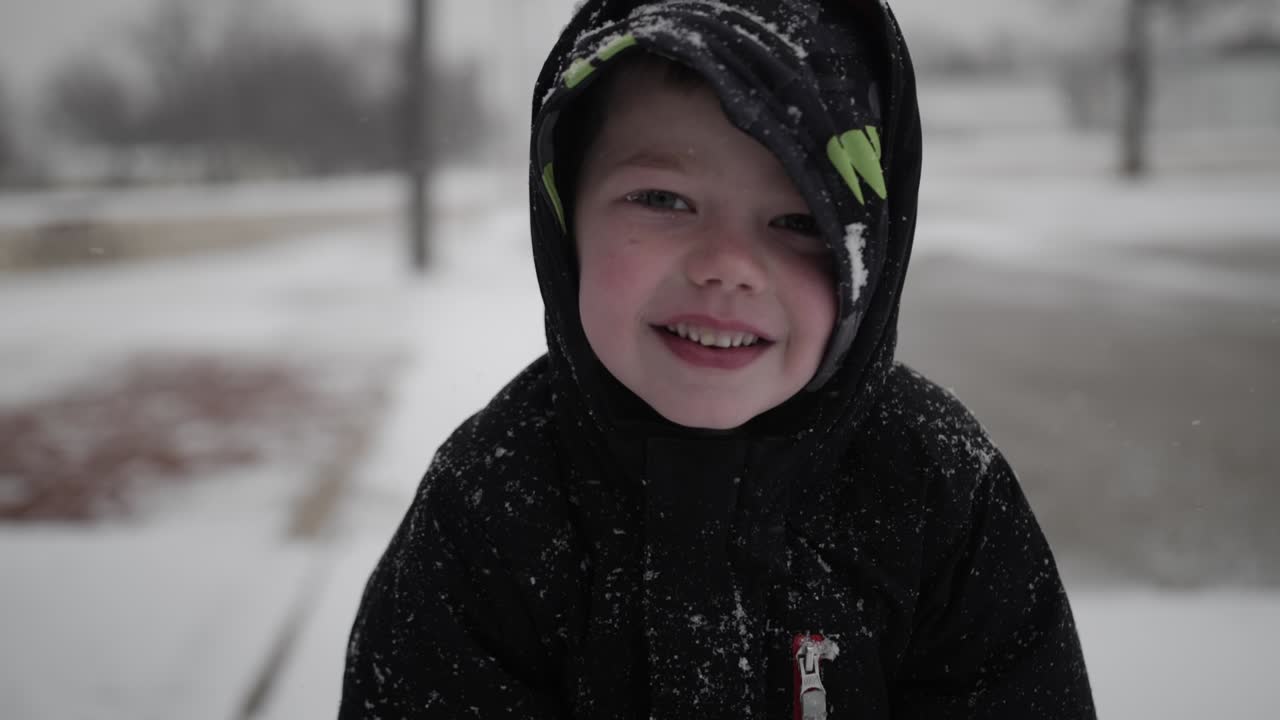 niño feliz sonriendo y usando un abrigo jugando afuera en un frío día de invierno en diciembre en la nieve durante las vacaciones de navidad en un pequeño pueblo en el medio oeste