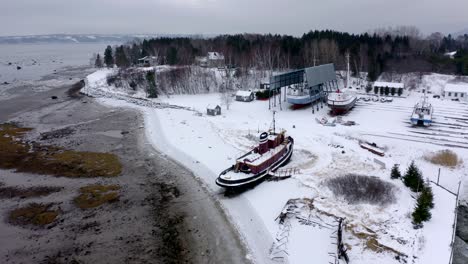 Drone-Volando-Alrededor-De-Un-Viejo-Barco-En-Invierno-En-Charlevoix,-Quebec