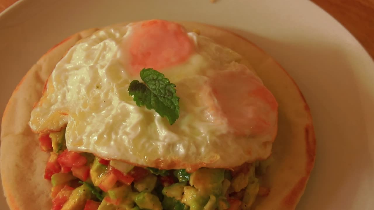 pan de pita con ensalada de tomates y aguacate cubierto con huevo frito para un desayuno vegetariano saludable
