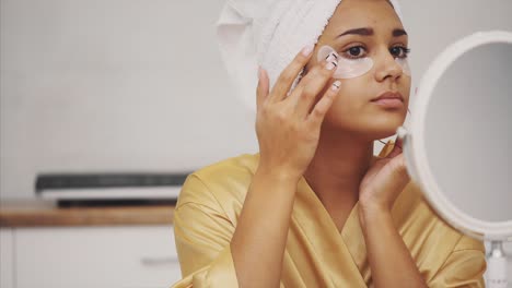 el retrato en primer plano de una mujer hermosa después de un baño con una toalla en la cabeza pone parches debajo de los ojos de arrugas y círculos oscuros.