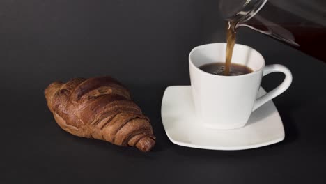 verter café de prensa francesa en una taza blanca junto a un croissant