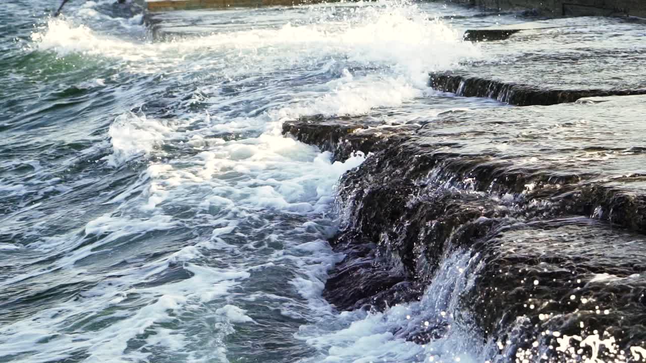 Water flowing over the rocky surface and waves are making white foam. Powerful ocean wave splashes across many rocks. Breathtaking view of breaking wave foaming on black rocks.