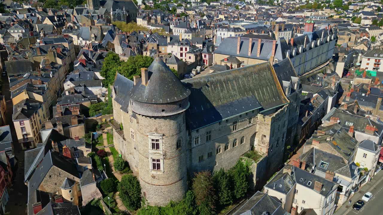 Drone footage beginning with close-up of medieval Château de Laval, highlighting its cylindrical towers, stone walls, and steep slate roofs then gradually pulling away to reveal surrounding townscape