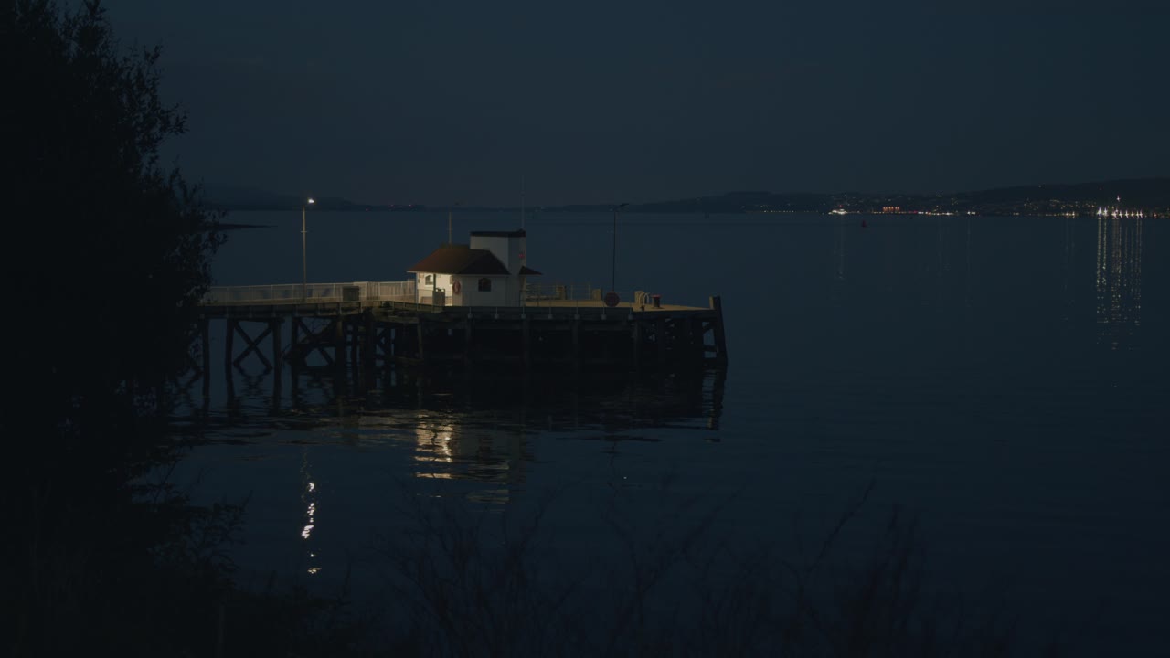 спокойный вечерний вид на старый викторианский пирс, его структура отражается в спокойных водах, с далекими городскими огнями и затемняющимся небом