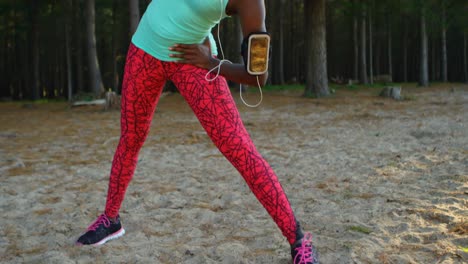 female athlete performing stretching exercise while listening music in forest 4k