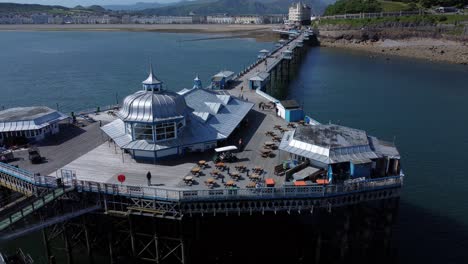 Llandudno-pier-seaside-resort-landmark-silver-pavilion-wooden-boardwalk-aerial-view-pull-back-reveal