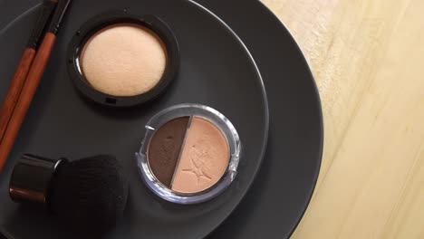 minimal concept background with make up, brushes and powders, on a grey plate, rotating on a wooden table