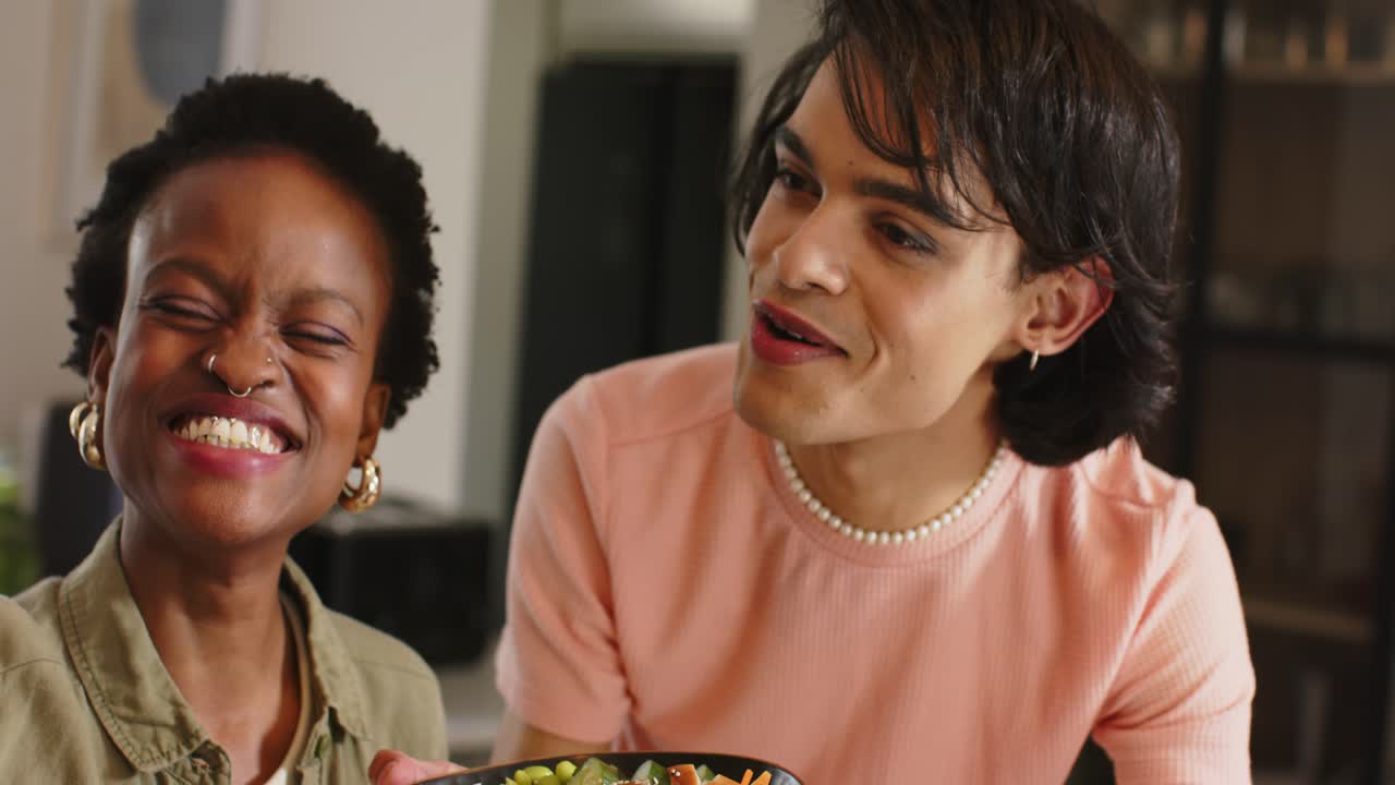 Camera panning back diverse friends holding salad bowl at counter, examining toppings and laughing