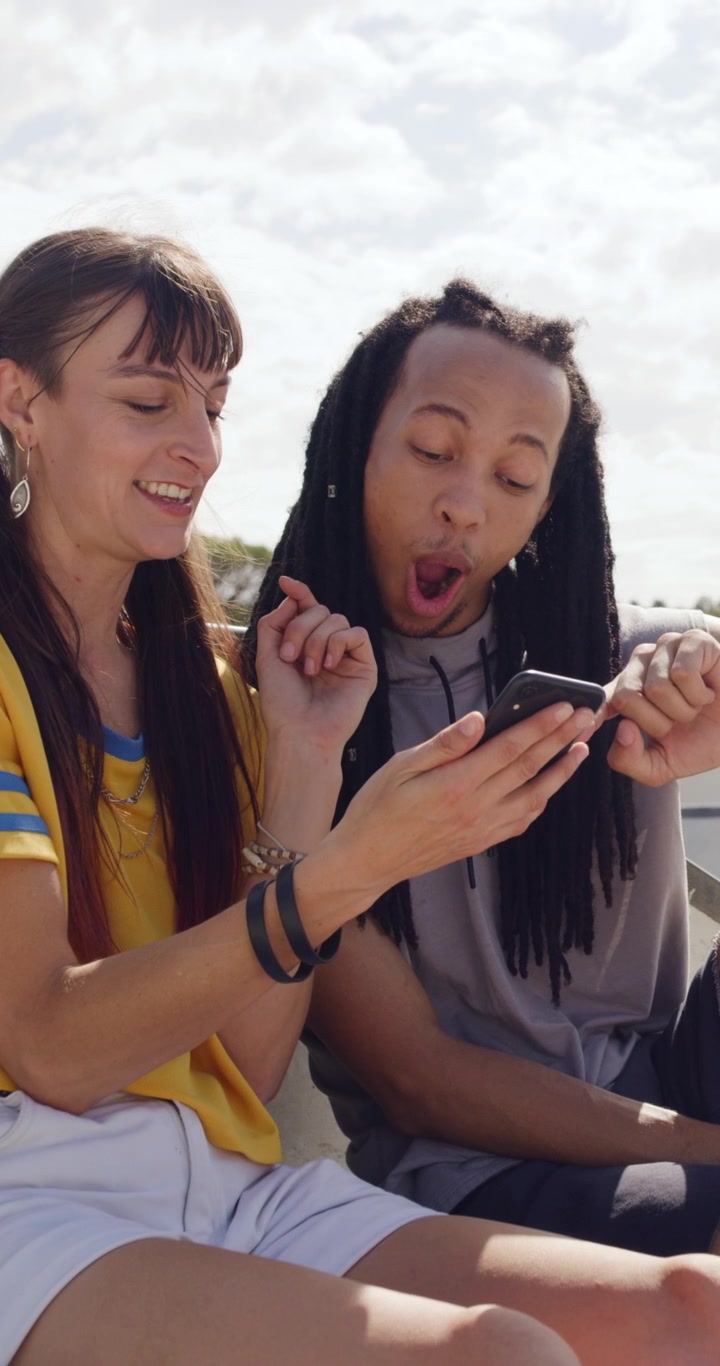 Young Couple Laughing and Looking at Smartphone Outdoors