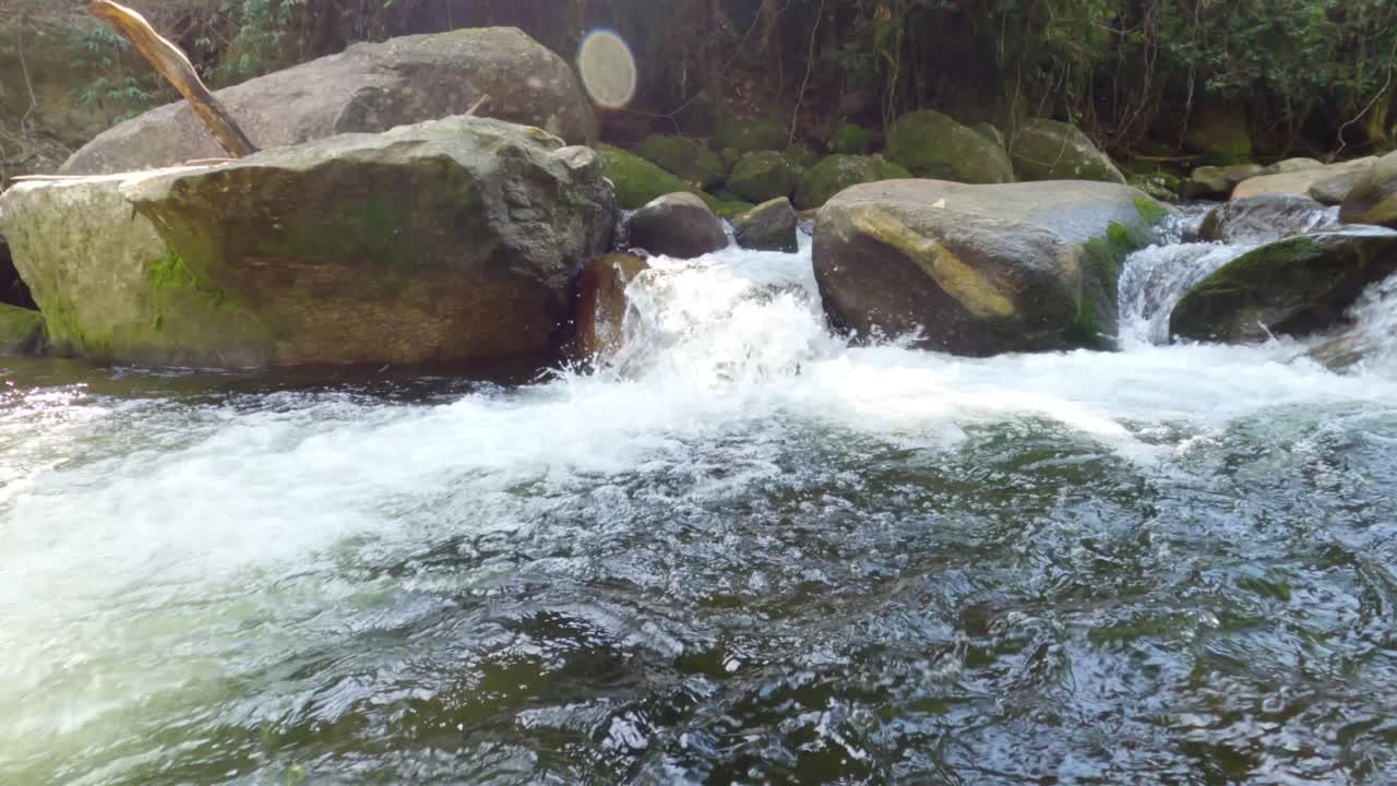 태양 반사와 함께 바위 사이를 흐르는 폭포 스트림의 슬로우 모션 비디오