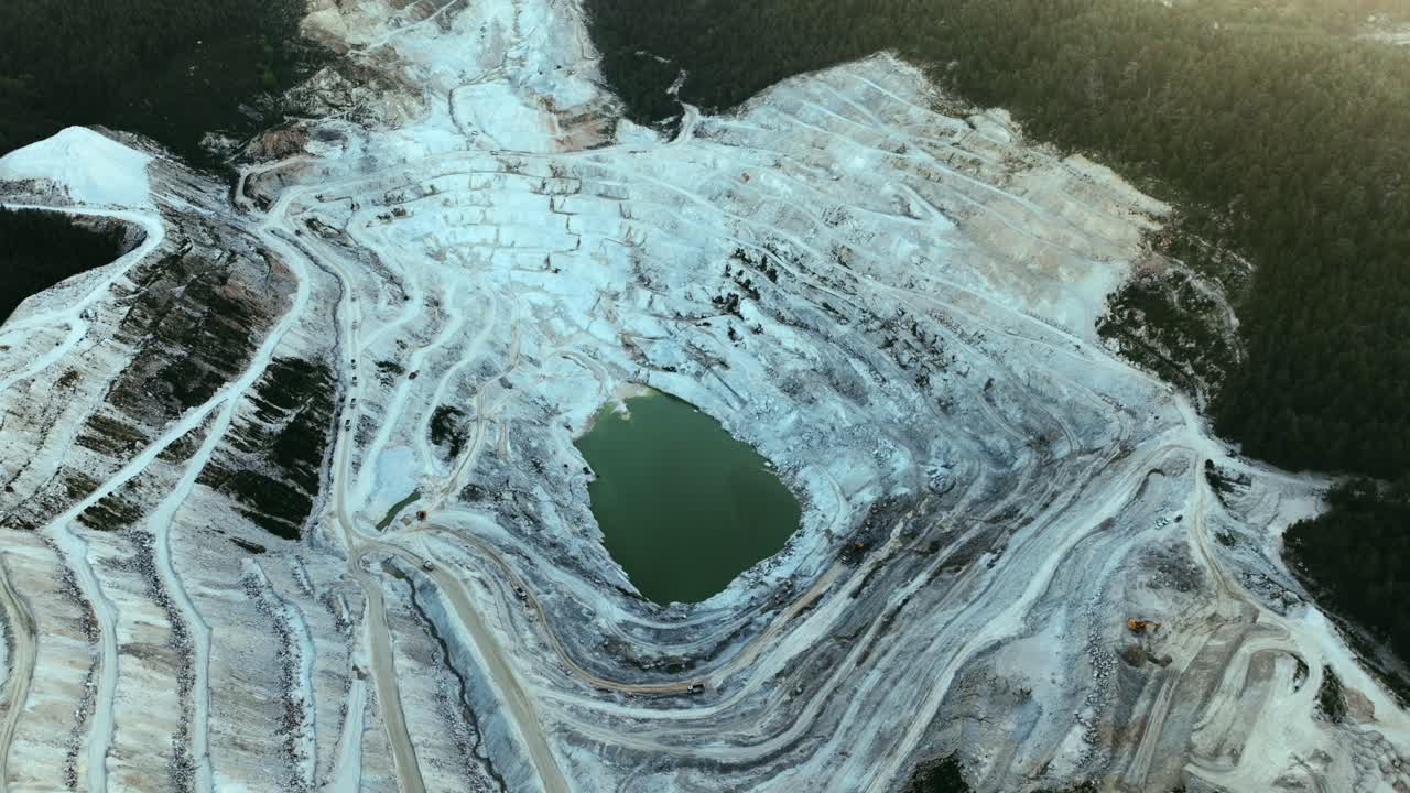 Aerial view of an expansive open-pit mining operation nestled in a forested area.