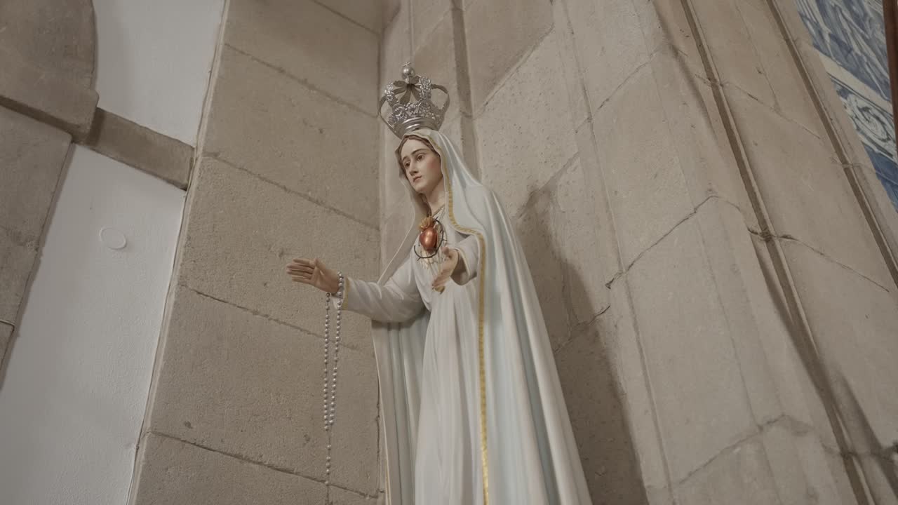 Close up of the statue of Our Lady of Fátima holding a rosary, displayed inside a stone church in Portugal
