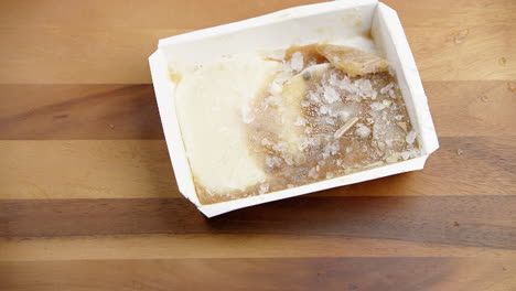 Comida-Congelada-Con-Hielo-En-Un-Recipiente-De-Comida-Que-Se-Arroja-Sobre-Una-Mesa-De-Comedor-De-Madera