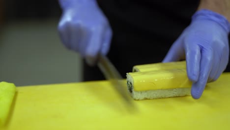 un cocinero corta cuidadosamente un rollo de sushi entero en pequeños trozos iguales