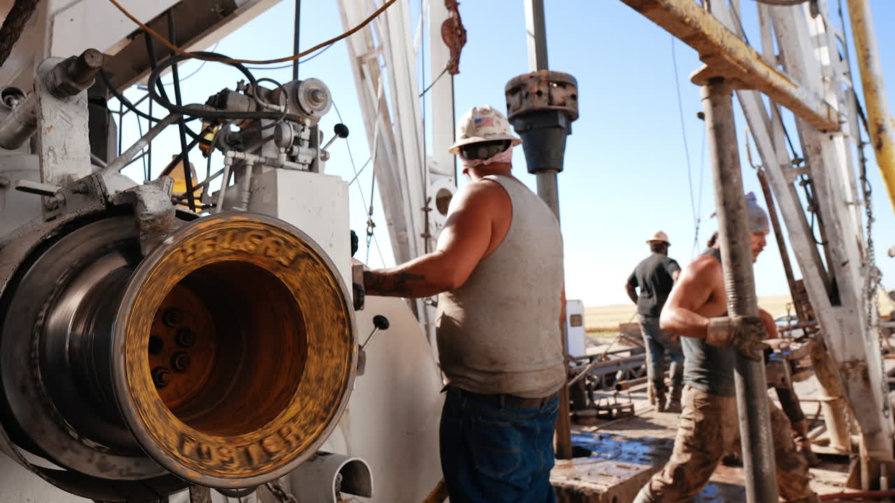 Male crew working with equipment at the oil drilling site. Bearded man comes up showing his muscles to the camera.