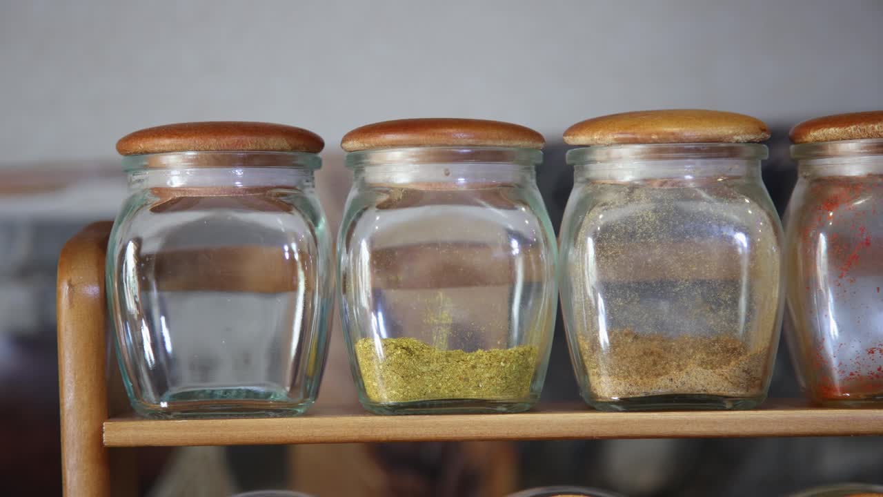 Organized kitchen spices in clear glass jars with wooden lids create a warm, inviting culinary atmosphere for cooking and baking content