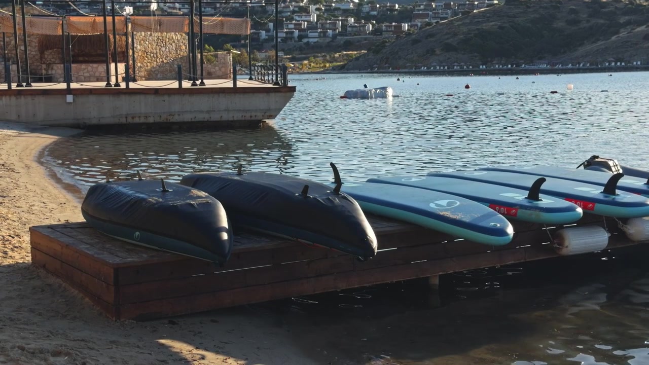 Overhead view of canoes and kayaks neatly stored at a calm lake dock shore with sunlight sparkling on the still water