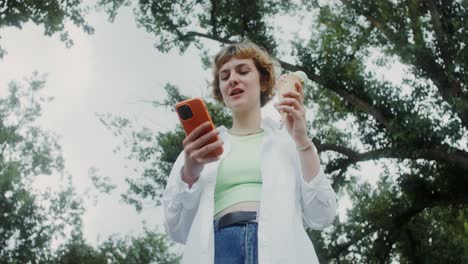 woman enjoying ice cream and smartphone in park