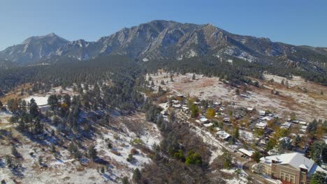 wide drone aerial shot of flatirons mountains covered in light snow on a fall day in boulder, colorado, usa