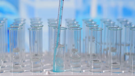 Scientist-injecting-chemicals-into-test-tubes.-Test-tube-of-colored-liquid-on-the-lab-table-in-the-background-of-the-glass-flasks.-poured-from-glass-pipette-into-test-tube-illuminated-with-blue-light.-High-quality-4k-footage