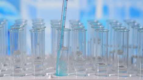 científico inyectando productos químicos en tubos de ensayo. tubo de ensayo de líquido de color en la mesa de laboratorio en el fondo de los frascos de vidrio. vertido de pipeta de vidrio en tubo de ensayo iluminado con luz azul. imágenes de alta calidad 4k