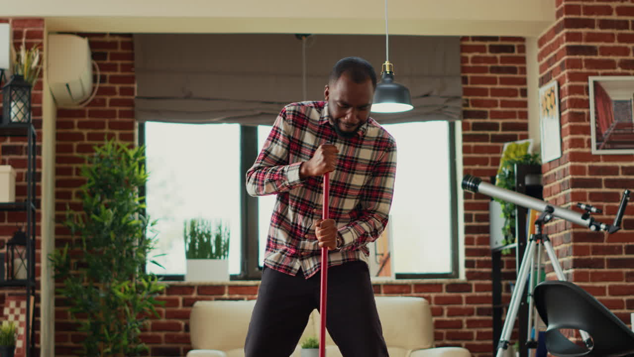 African american adult mopping living room wooden floors and dancing