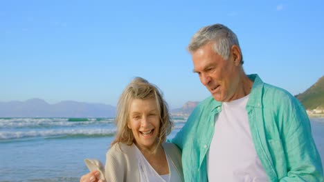 Front-view-of-senior-Caucasian-couple-holding-a-seashell-on-the-beach-4k