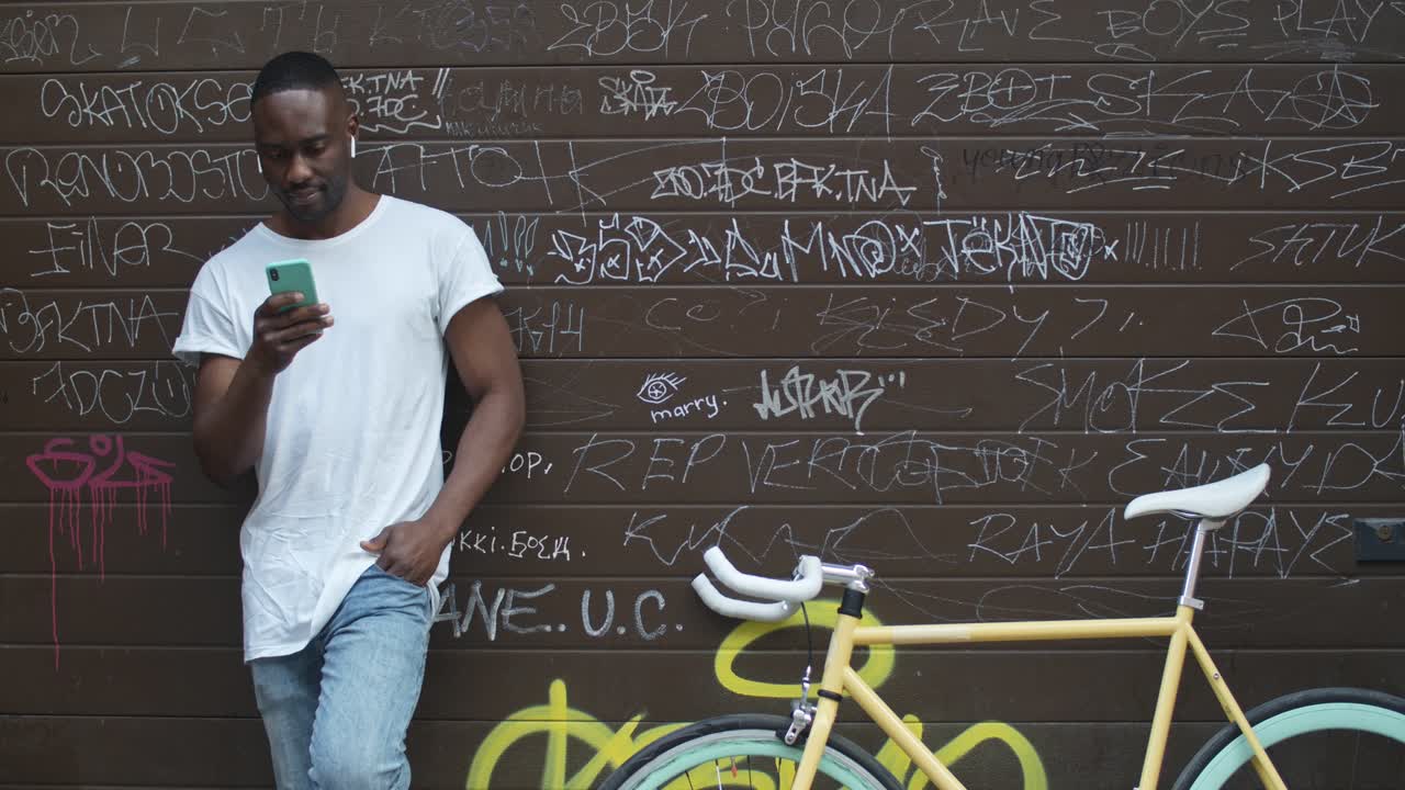 Man with bicycle using phone against graffiti wall