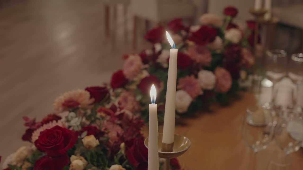 Intimate glow of taper candles nestled in lush red and pink blooms for elegant dining