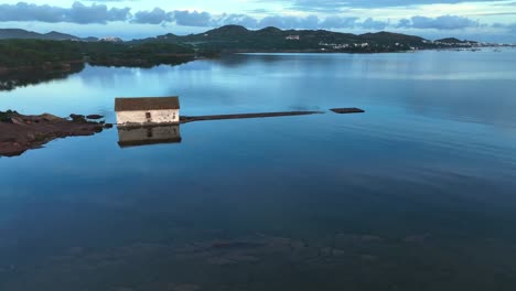 Drone-footage-of-calm-ocean-bay-in-Spain-with-old-boat-house-sitting-on-the-coastline