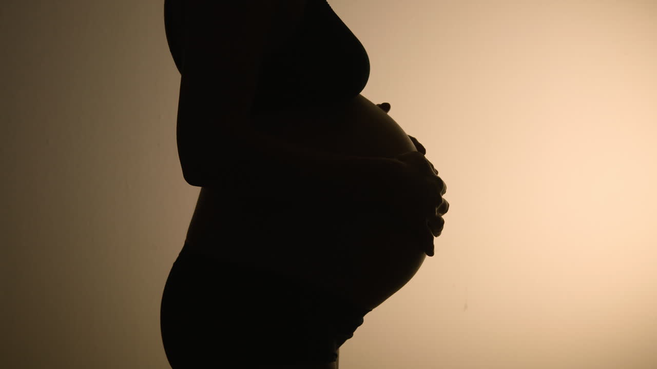 A very pregnant belly close to giving birth, in silhouette against a wall