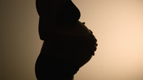 a very pregnant belly close to giving birth, in silhouette against a wall