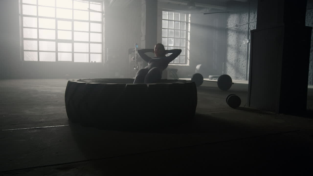복부 운동을 하는 소녀 체육관에서 타이어에 crunches. 복부를  ⁇ 핑하는 여자