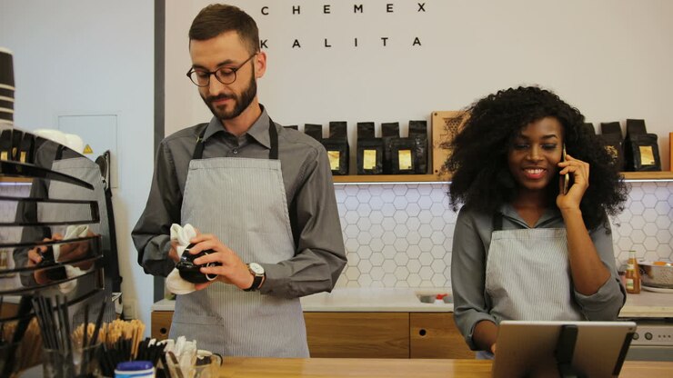 Caucasian barista with beard and african american young woman working in trendy coffee shop