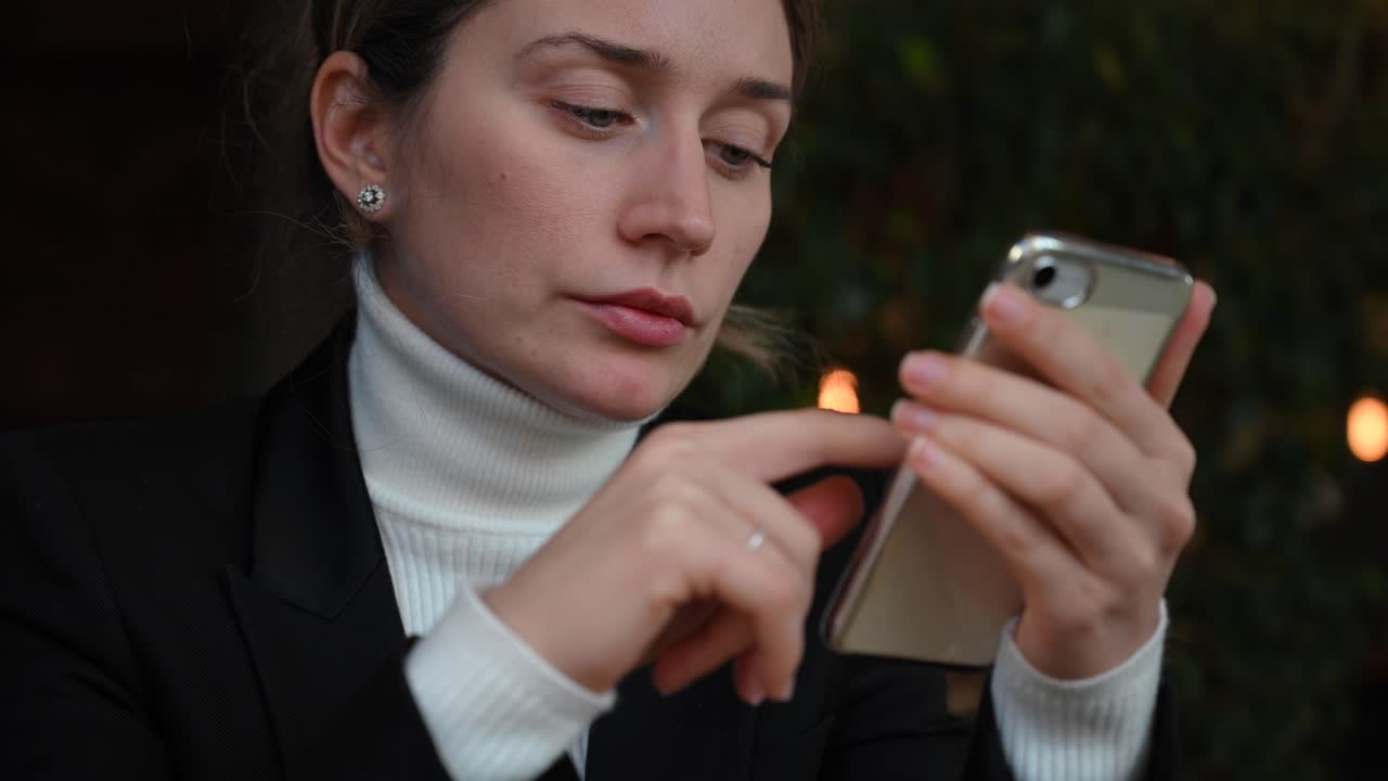 Close up of a brunette woman in a white turtleneck scrolling through her phone