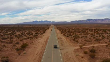 aéreo, volando detrás de un jeep conduciendo por una autopista en el épico paisaje del desierto de mojave